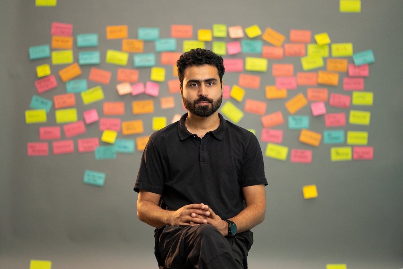 Portrait of Bilal Ismat in his studio, in front of a wall of colourful notes.